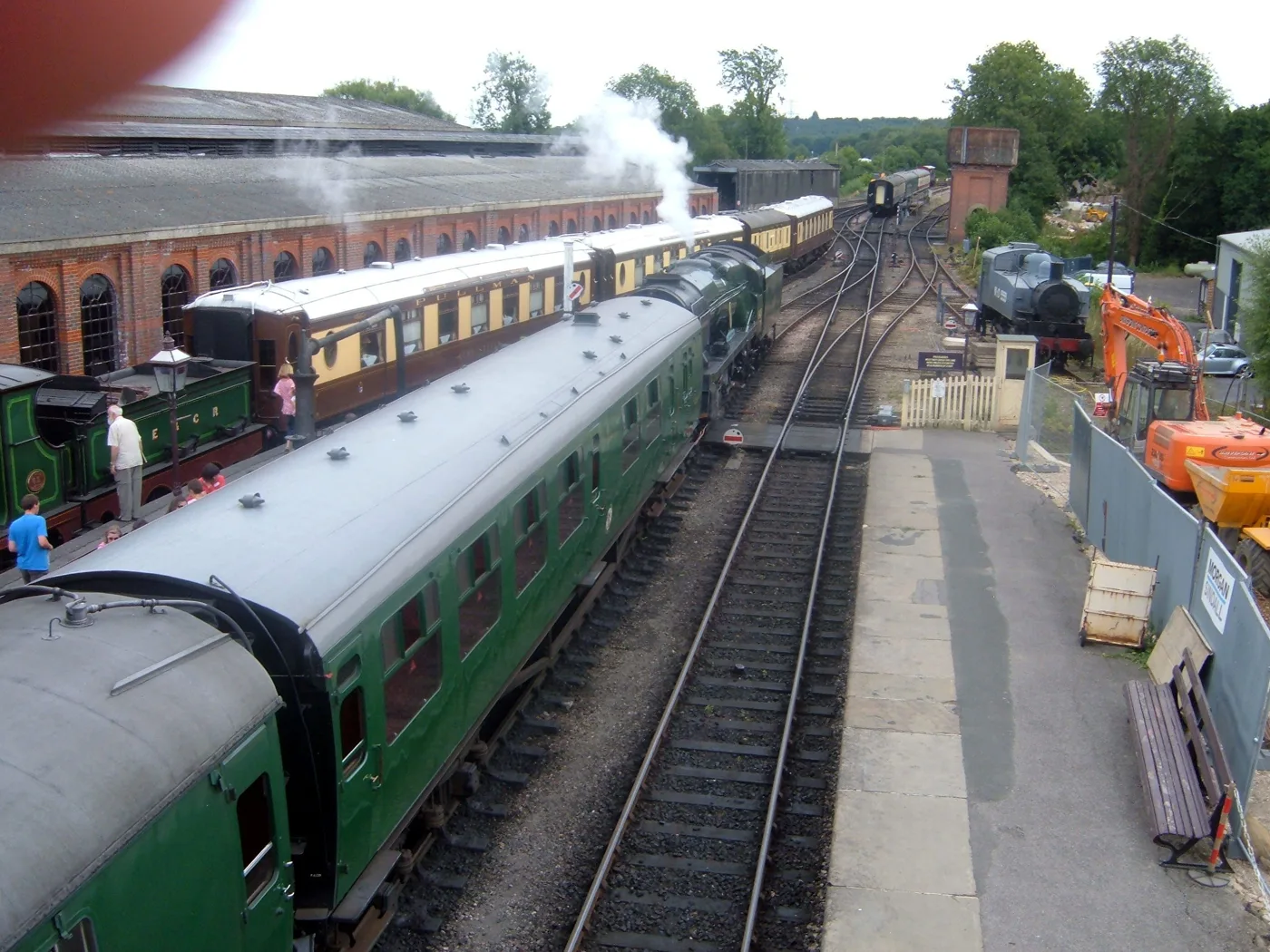 Visitors on the platform at Sheffield Park station on the Bluebell Railway, with a green carriage alongside and the red-brick station building behind