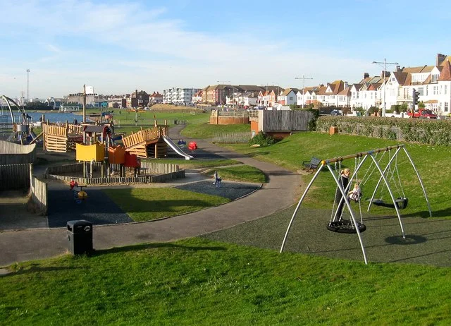 The children's playground at Hove Lagoon, with wooden climbing frames and a slide on the left and a row of swings on the right