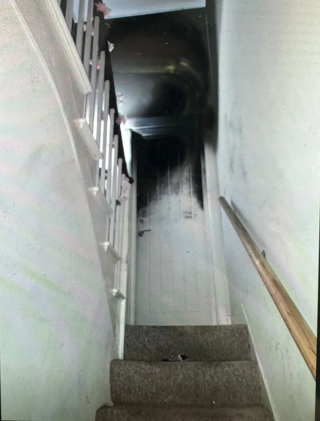 Looking up a carpeted staircase to a door with heavy black smoke staining on it and the ceiling above