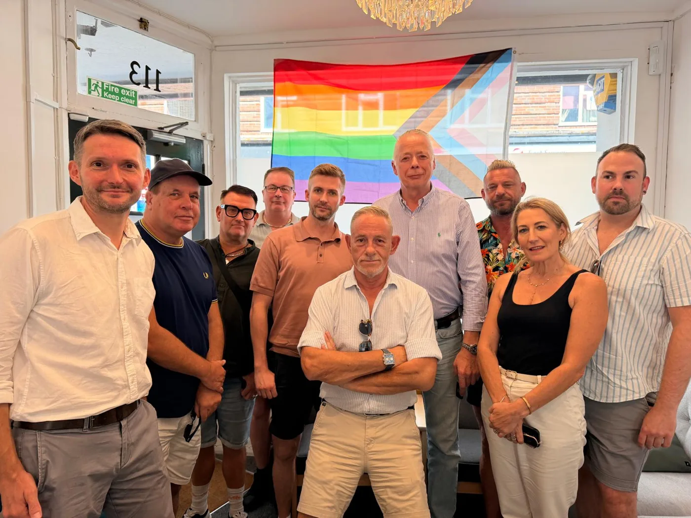 Chris Ward MP with LGBTQ+ business owners in front of a Progress Pride flag