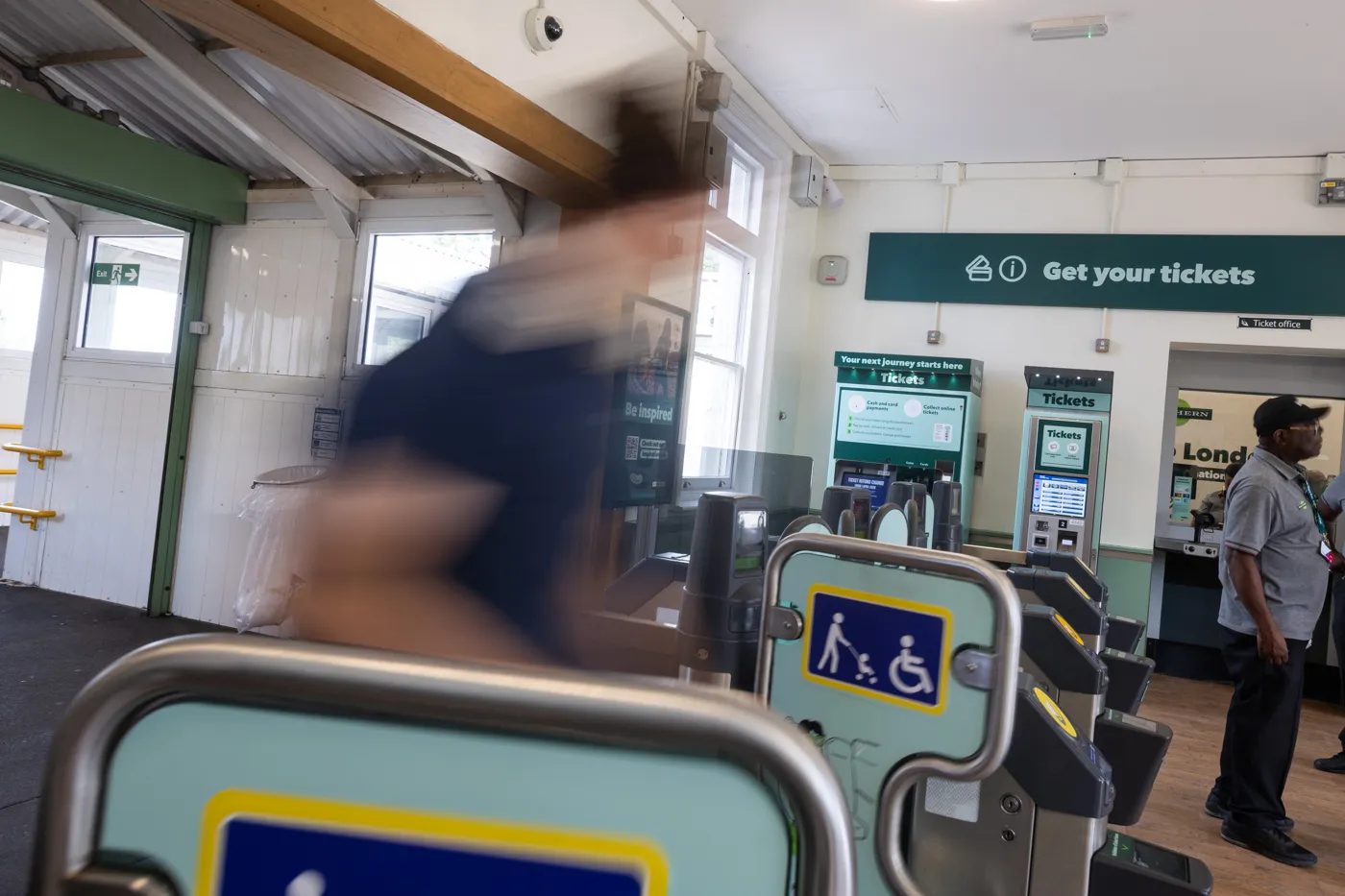 Ticket gates and ticket machines in a station booking hall, with a member of staff standing by the ticket office