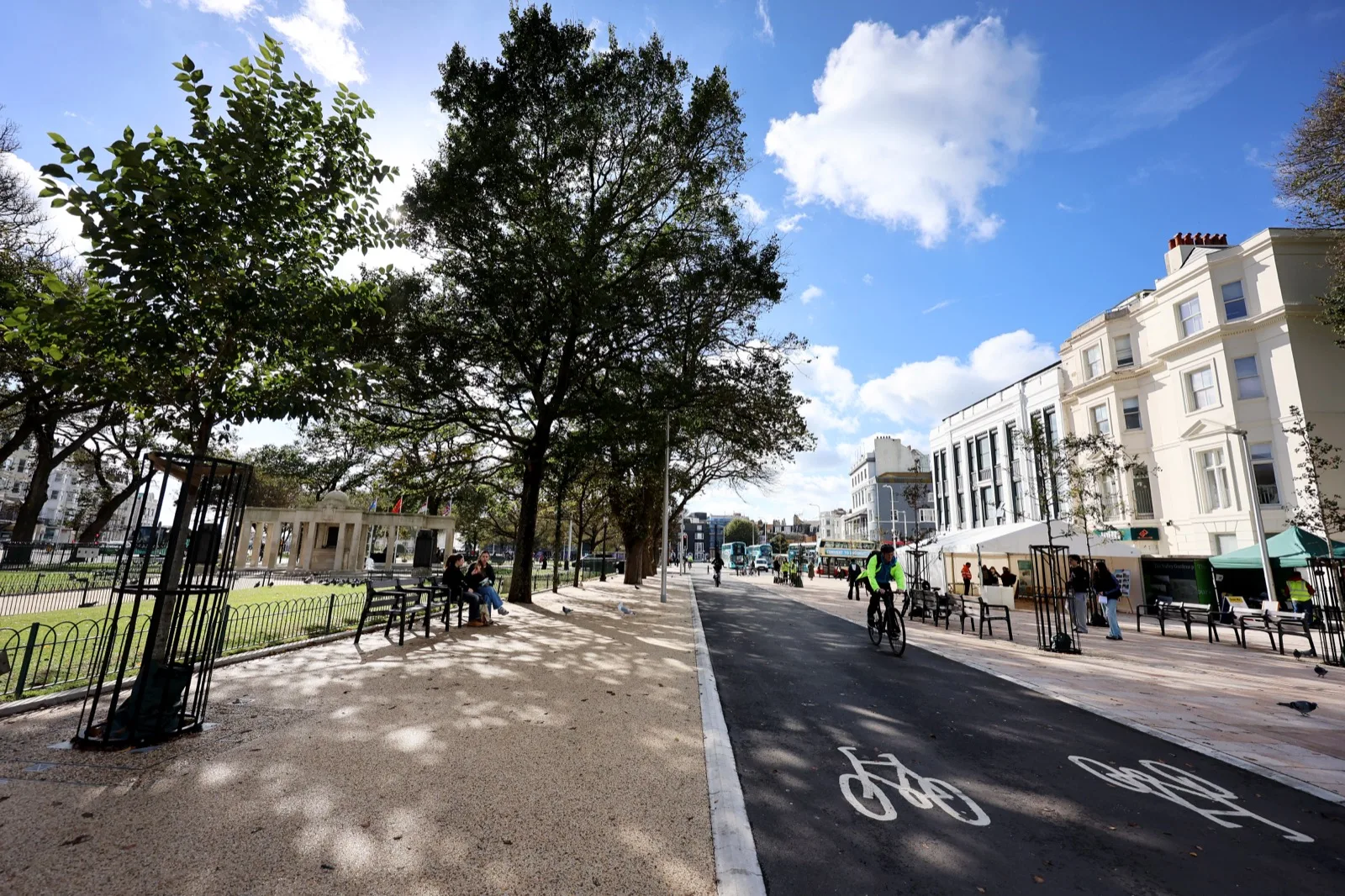 A cyclist on the new separated cycle lane beside the Old Steine in Brighton, with a wide resin path and new benches on the left, the War Memorial behind railings, and Regency terraces on the right